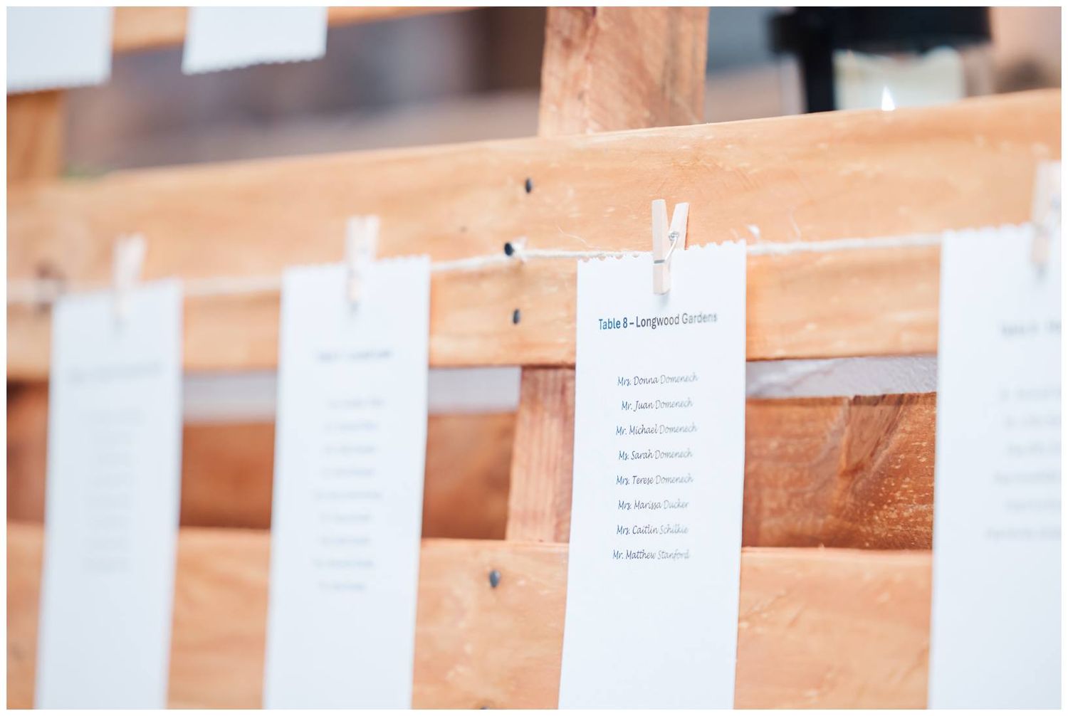 Wedding seating arrangements clipped to wooden boards with miniature clothespins.
