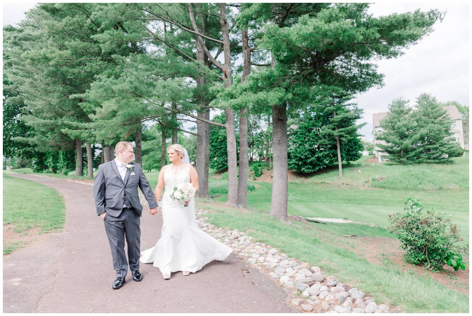 A couple walks hand in hand down a winding garden path surrounded by lush evergreen trees and landscaping.