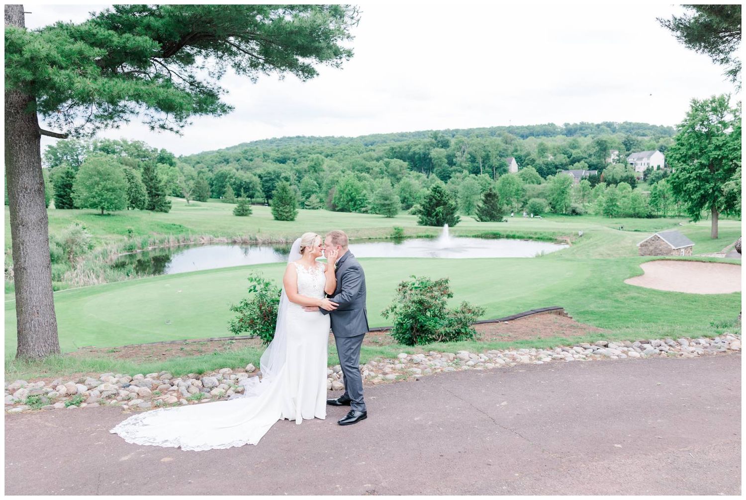 Two people share an intimate moment on a path overlooking a scenic golf course with rolling hills and green landscape.