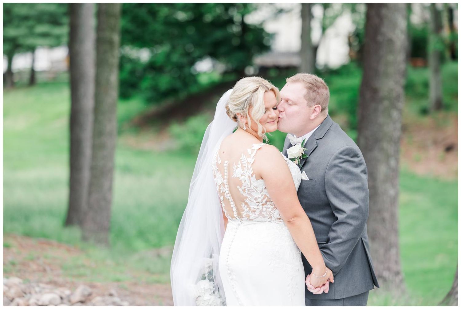 A romantic wedding couple shares a tender moment outdoors in a natural wooded setting.
