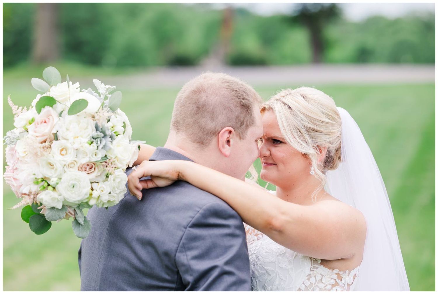 Romantic wedding couple sharing an intimate moment outdoors with the bride holding a white floral bouquet.