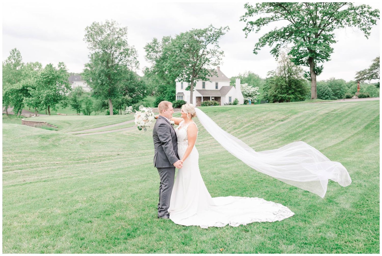 A romantic wedding portrait on a rolling green lawn with a flowing white veil caught in the breeze.