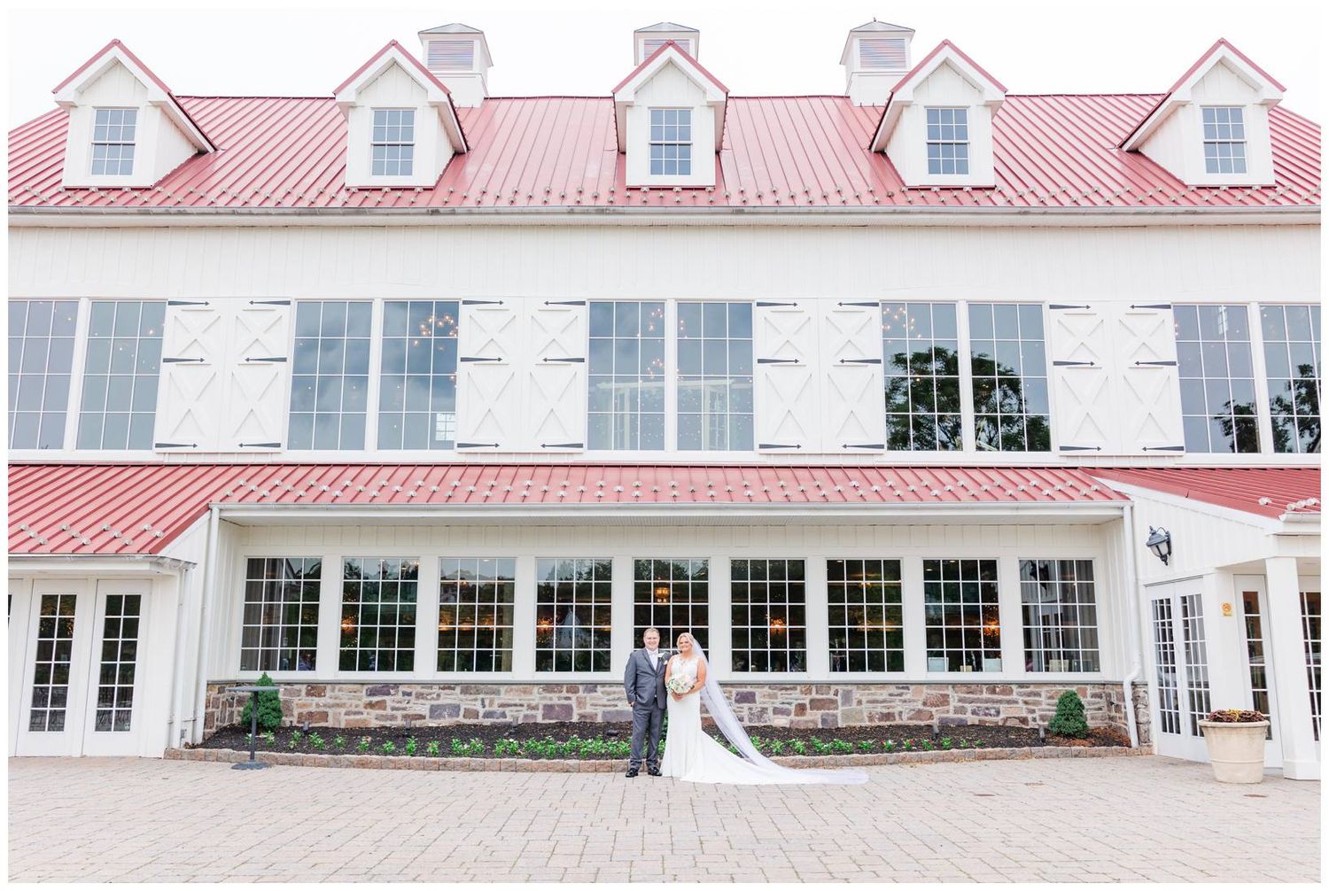 Elegant white colonial-style building with red roof and dormers provides a classic wedding venue backdrop.
