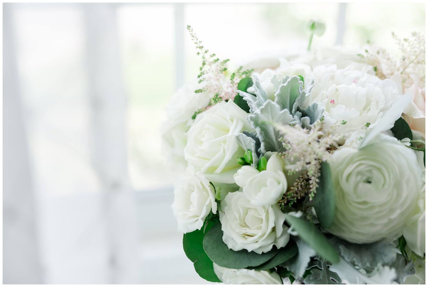 Close-up of elegant white rose and ranunculus bouquet with green accents in soft natural light.