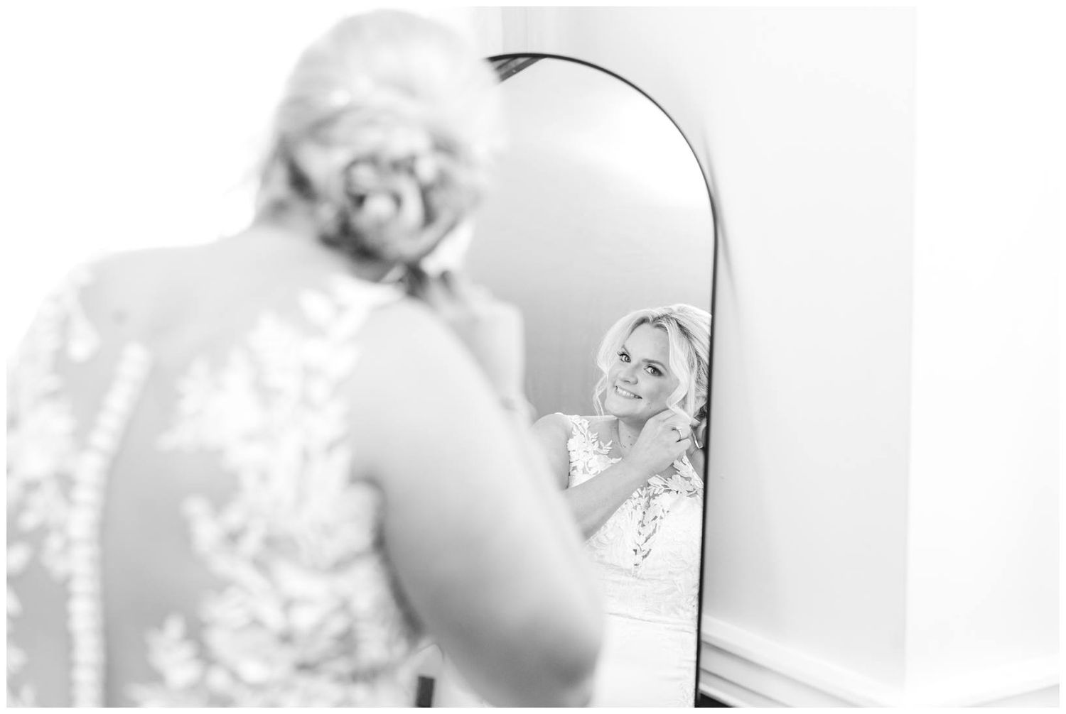 A black and white reflection in a mirror shows someone in a lace dress getting ready.