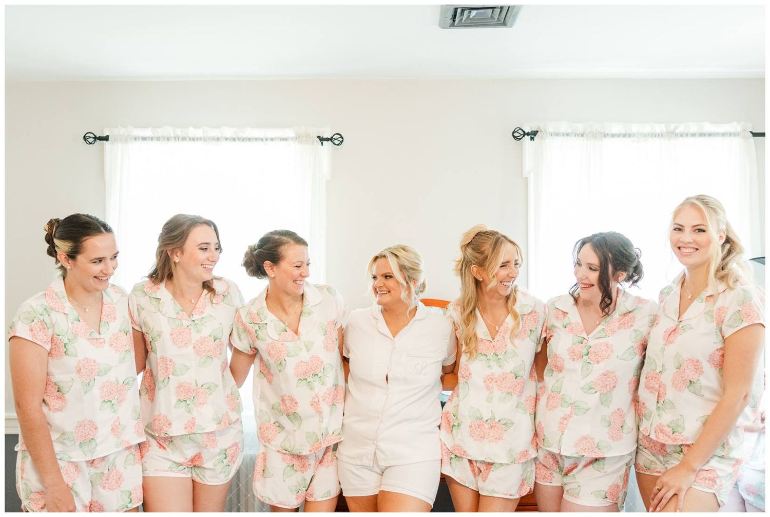 A group in matching floral print pajama sets pose together while laughing and smiling during a pre-wedding celebration.