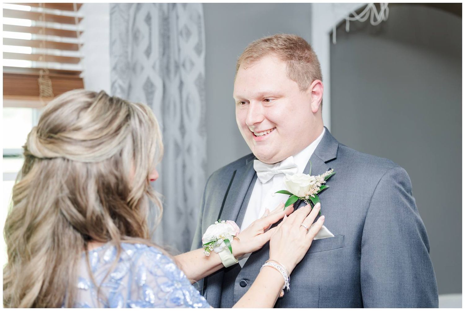 Someone pins a white floral boutonniere onto the lapel of a man wearing a gray suit at a formal event.