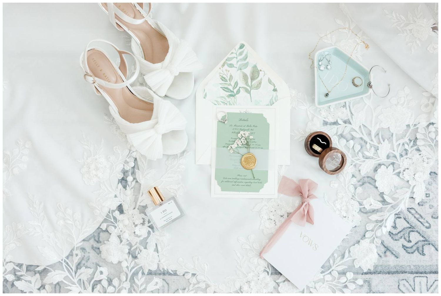 Flat lay of wedding accessories including white shoes, floral invitations, and silver lace details against marble background.