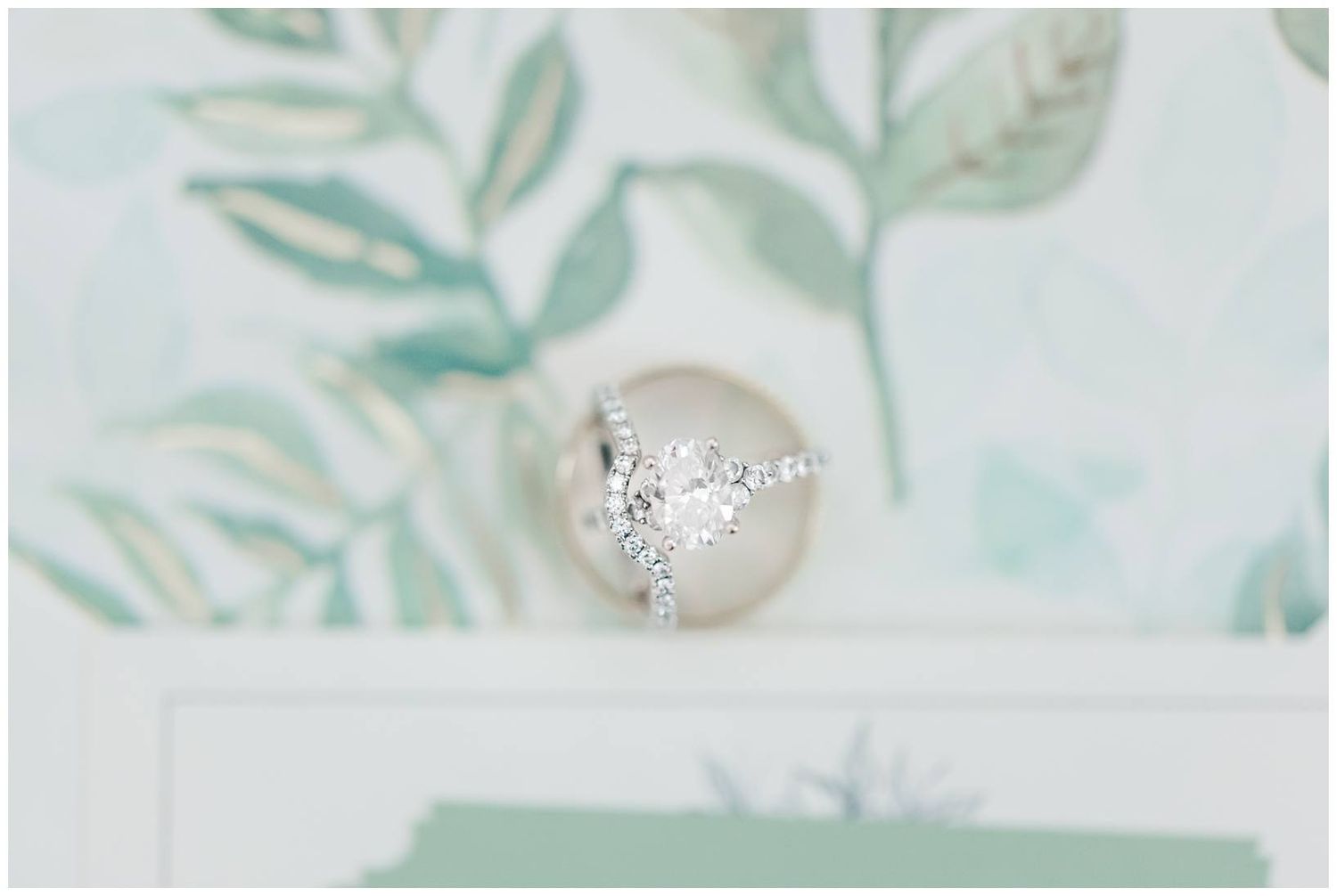 A sparkling diamond engagement ring sits elegantly against a soft mint green floral background.