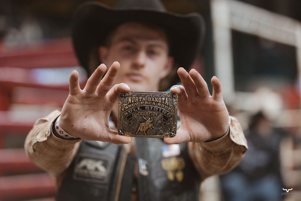 Rodeo participant holding up champion belt buckle trophy at competition.