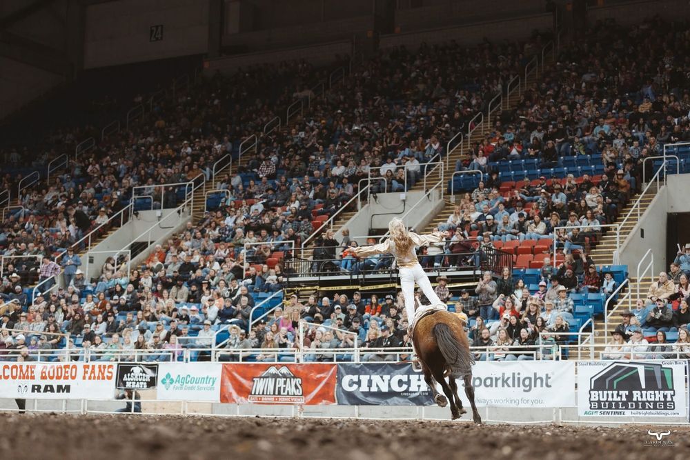 Bull rider performs at a packed rodeo arena with spectators watching in the background.