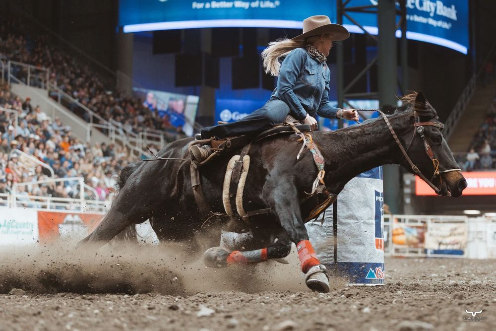 Cowboy competing in barrel racing event kicks up dust in indoor rodeo arena.