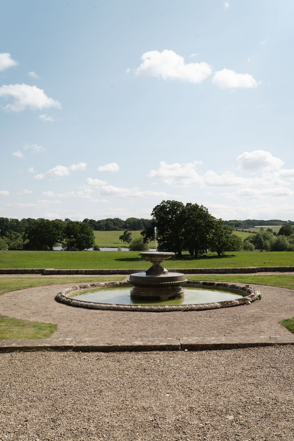 Circular stone fountain in manicured garden with rolling countryside views.