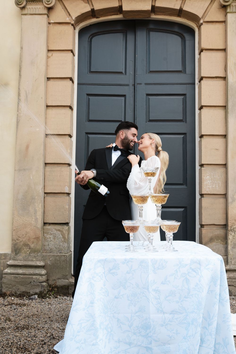 Couple posing by champagne tower near elegant doorway during wedding celebration.
