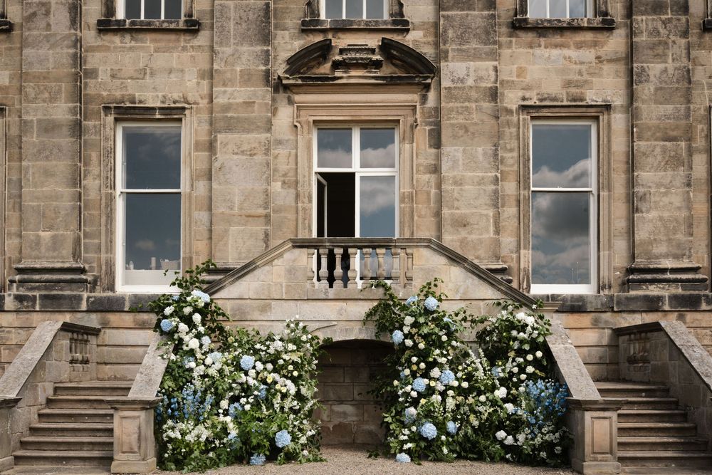 Historic stone building exterior with white flowering bushes and grand entrance steps.