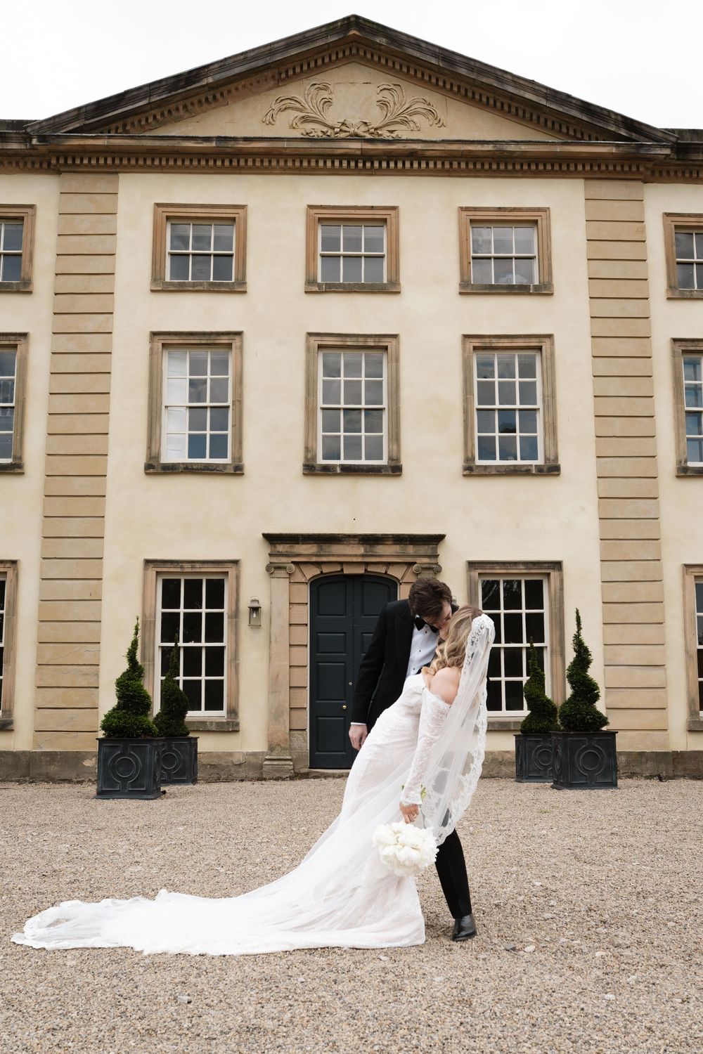 Elegant neoclassical building facade with long wedding dress train flowing across courtyard.