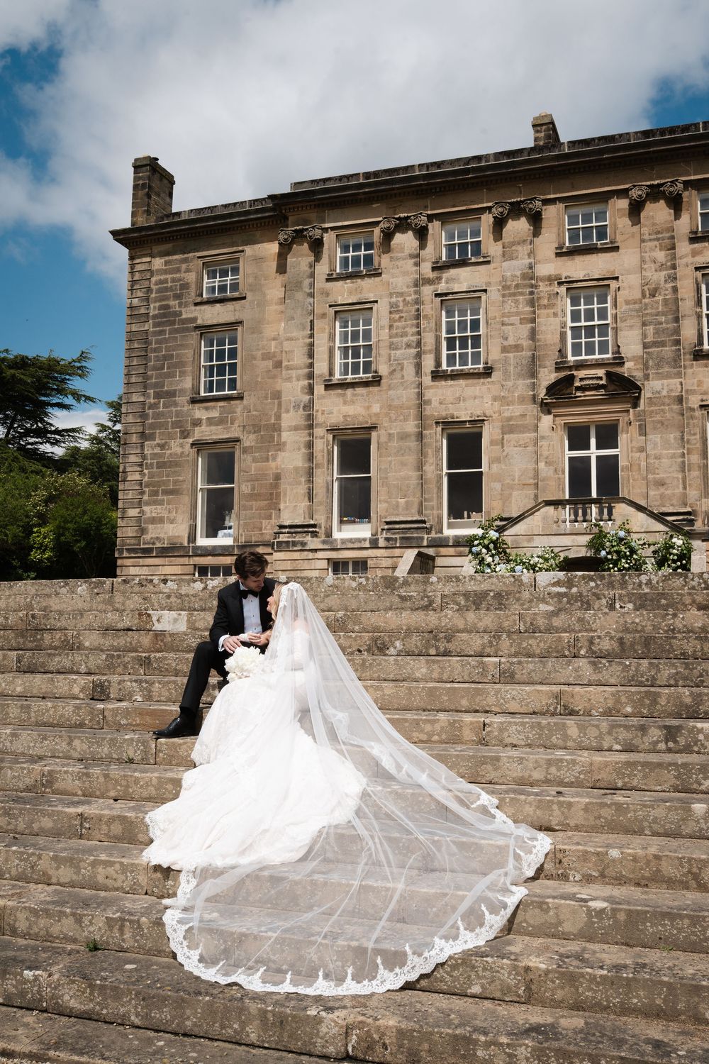 Long white bridal veil cascades down stone steps of stately manor house.