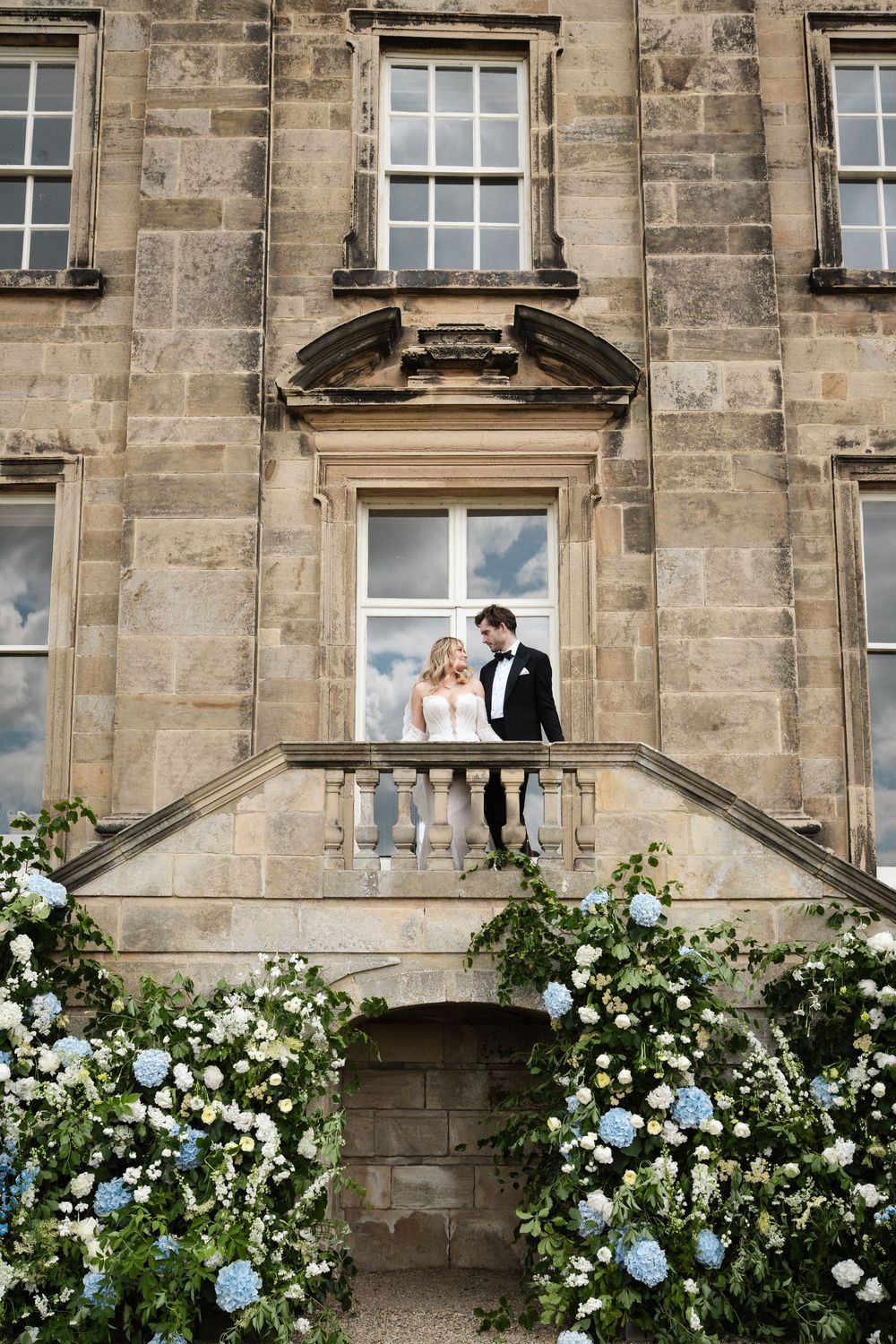 Couple stands on ornate balcony decorated with blue and white flowers.