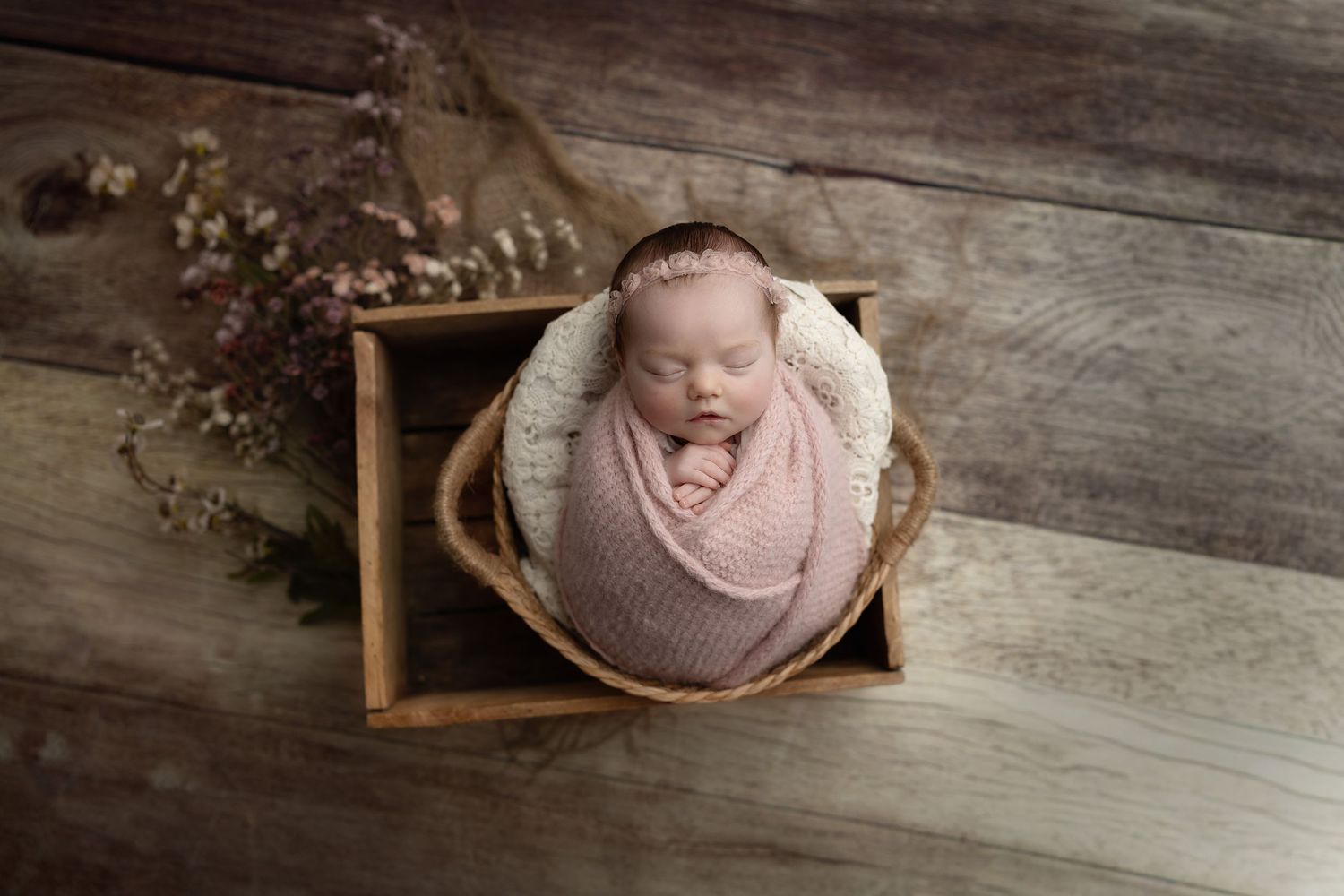 Ein neugeborenes Baby schläft in einem rustikalen Korb, umgeben von Blumen.