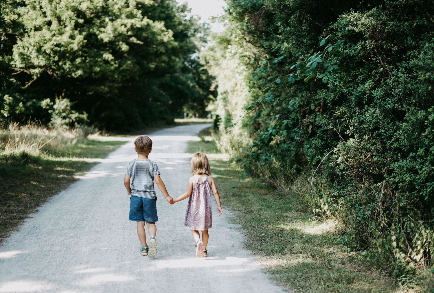 Zwei kleine Kinder laufen händchenhaltend einen Weg in der Natur.