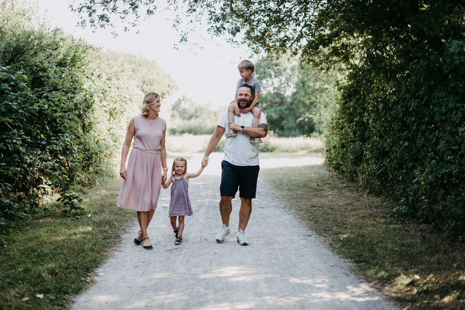 Eine Familie spaziert auf einem Waldweg. Die Mutter hält die Hand der Tochter, während der Vater den Sohn auf den Schultern trägt.