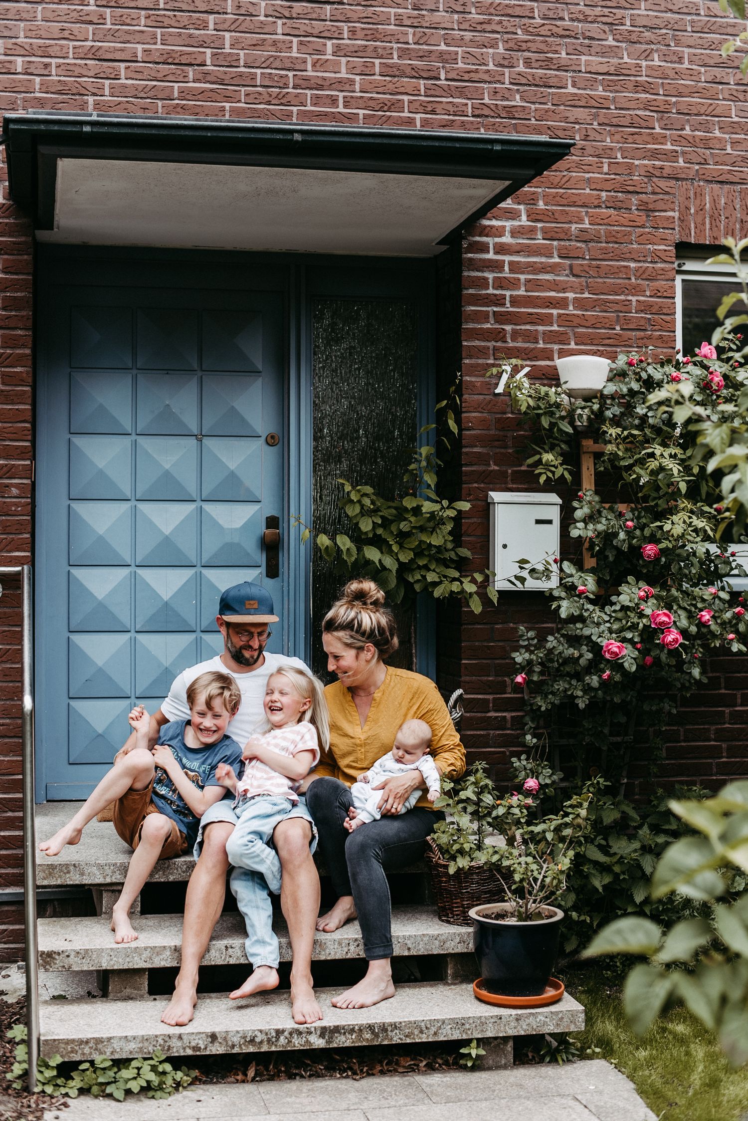 Ein Portrait einer Familie. Die Familie sitzt vor ihrer blauen Haustür. Die Kinder sitzen auf dem Schoß ihrer Eltern.