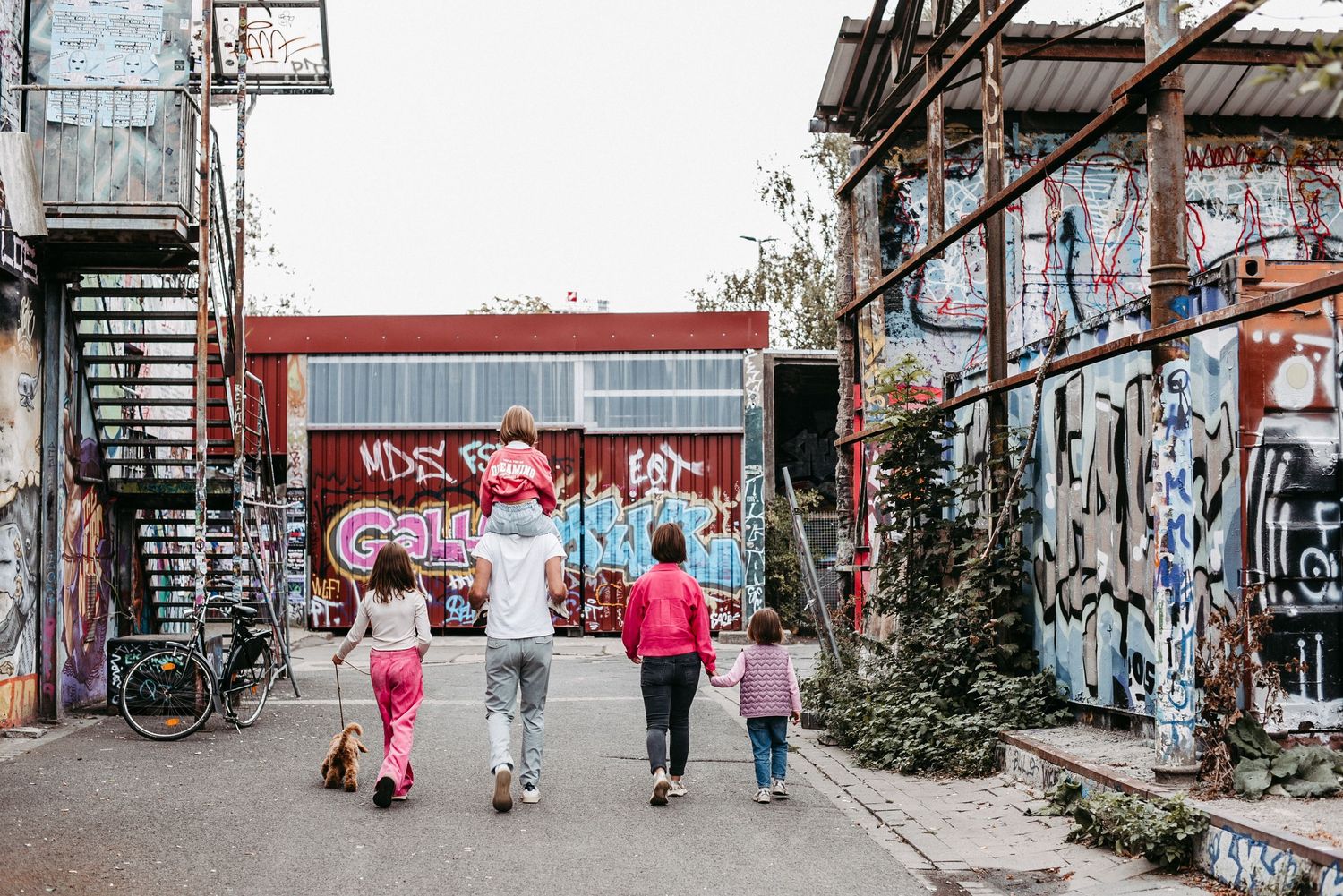 Eine Familie spaziert durch eine mit Graffiti bedeckte Straße. Ein Kind sitzt auf den Schultern eines Erwachsenen.