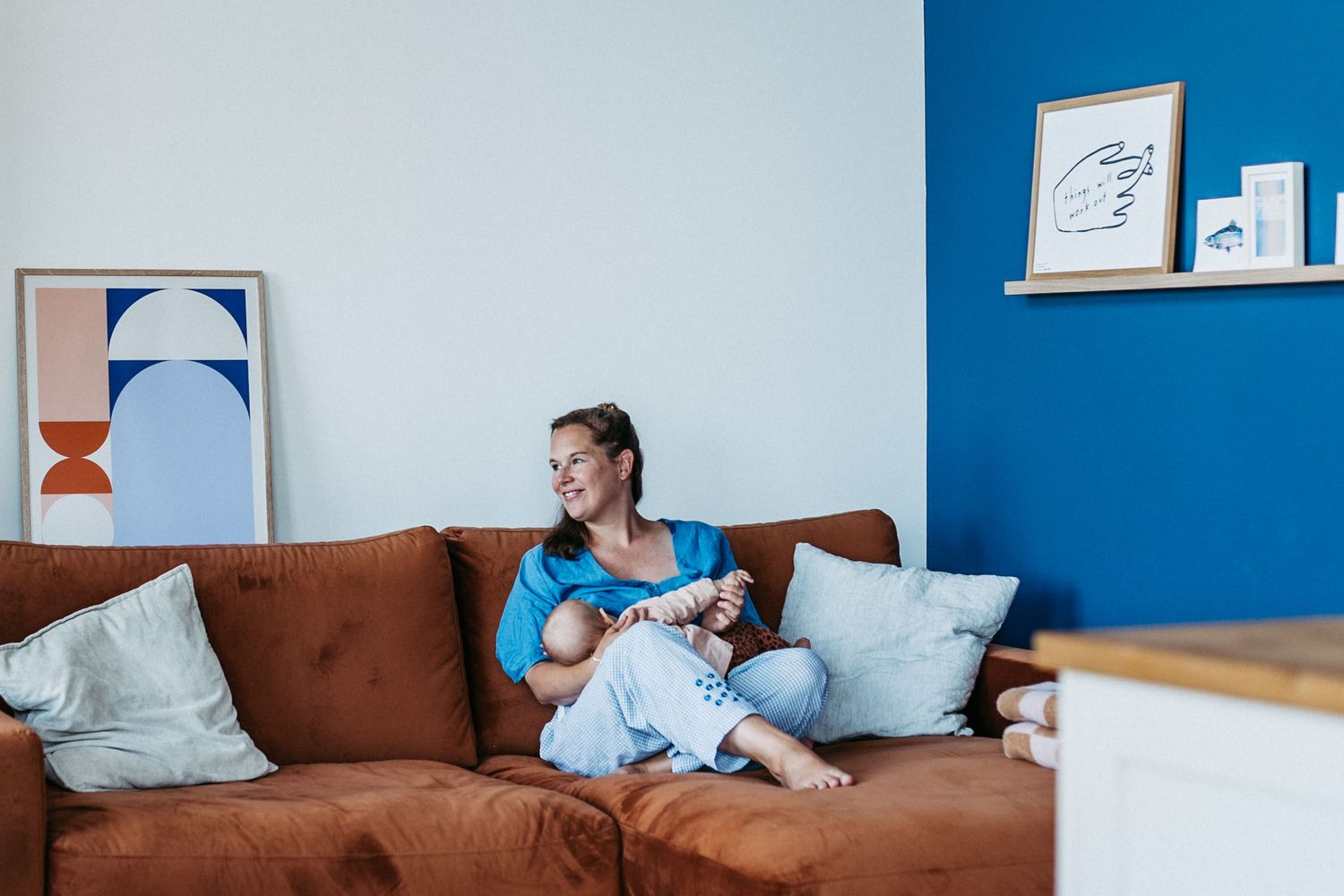 Frau sitzt lächelnd auf einem braunen Sofa in einem modern eingerichteten Raum mit blauen und weißen Wänden und Kunstwerken.