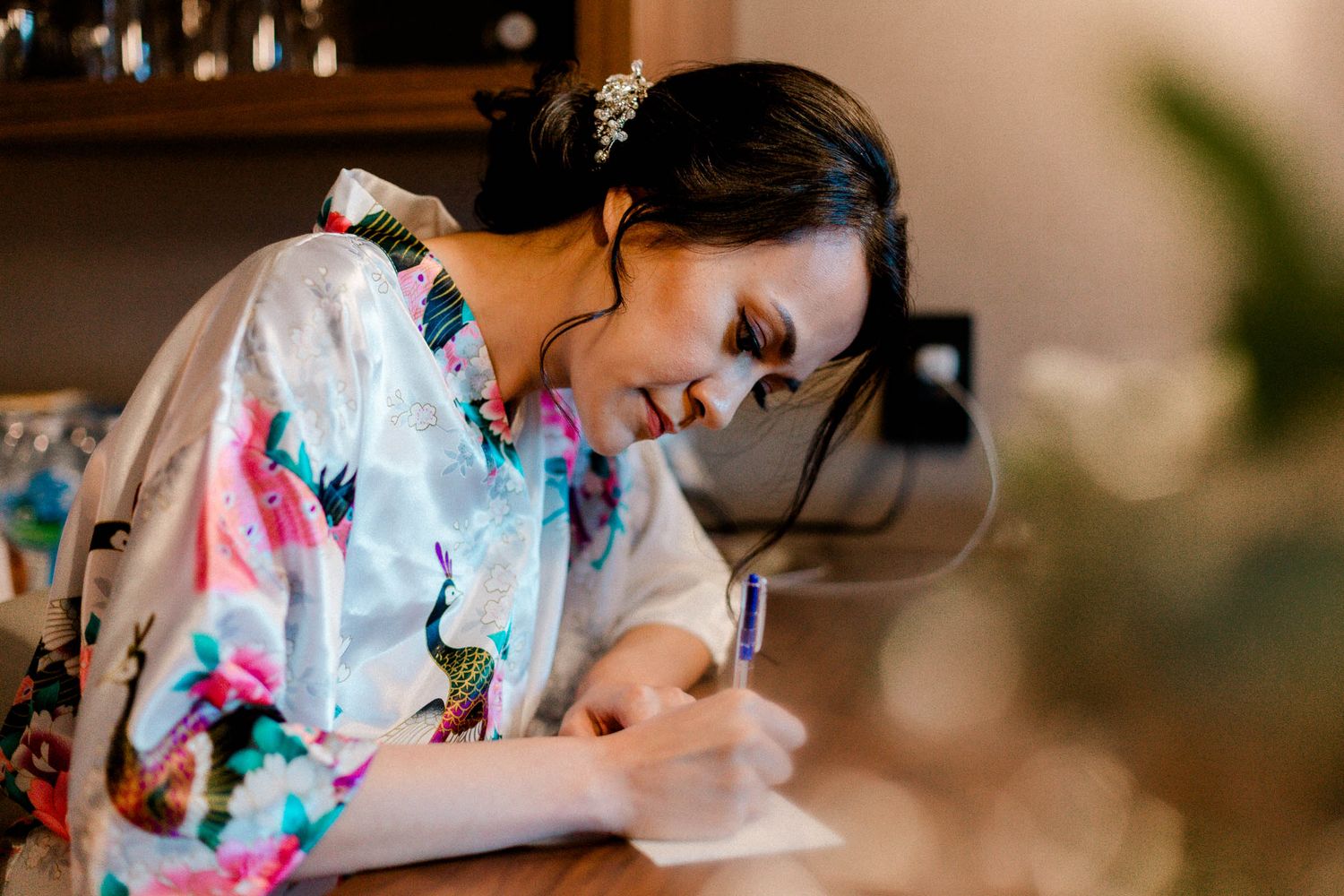 The bride wearing colorful floral robe writes the vows when getting ready in a cozy indoor setting.