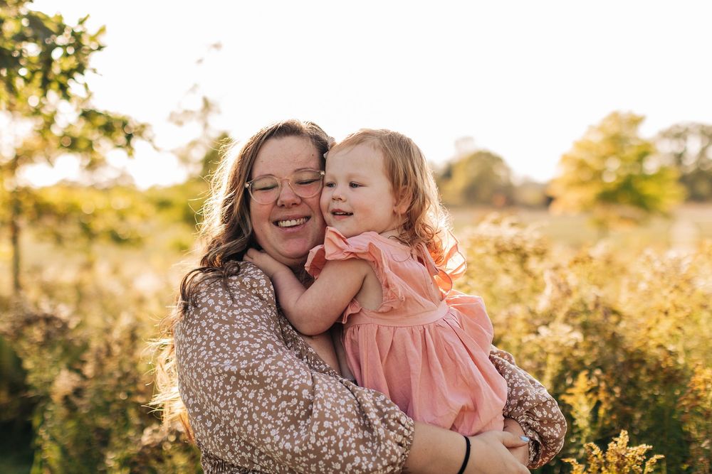 Two people sharing a joyful embrace outdoors during golden hour in a sunny field with vegetation.