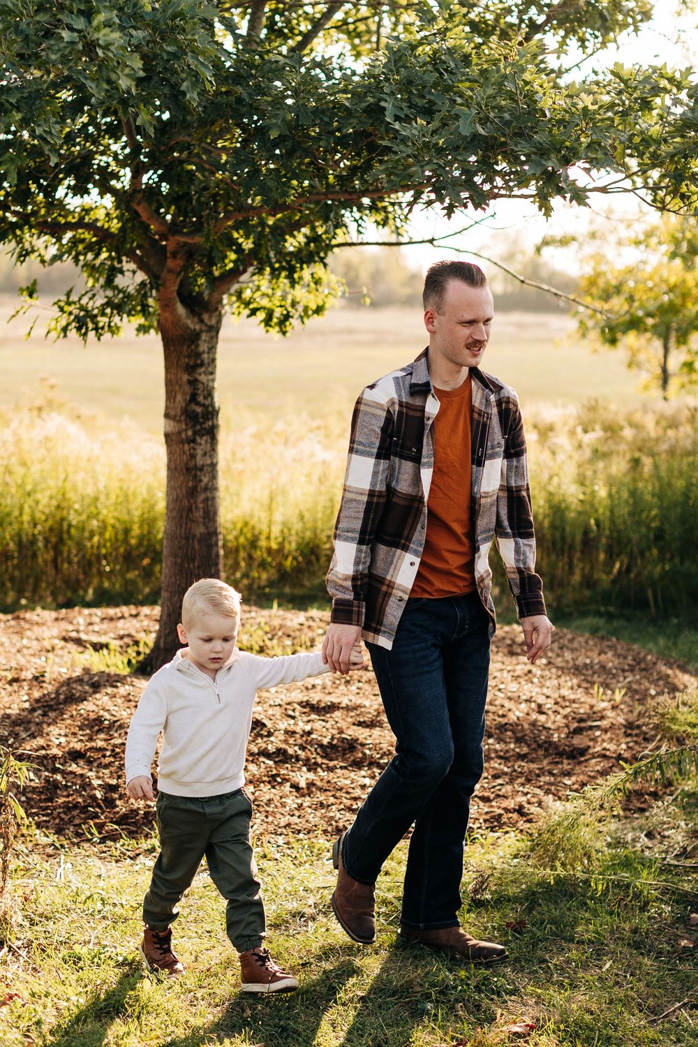 Two people walking together in a sunlit field with trees in the background during golden hour.