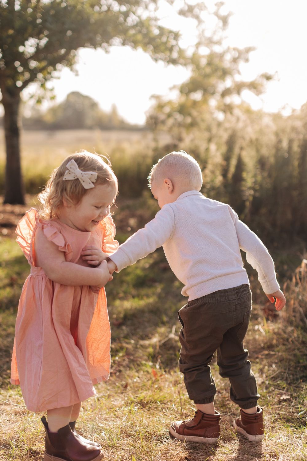 Two children playing outdoors at sunset, with a girl in a peach dress and boy in white sweater.