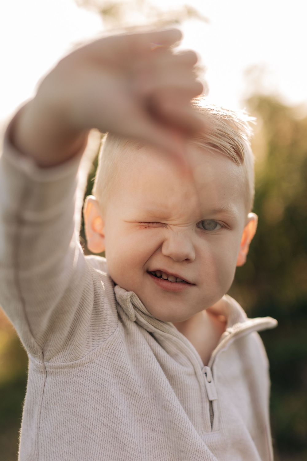 Close up portrait of happy toddler wearing beige sweatshirt reaching up outdoors in golden sunlight.