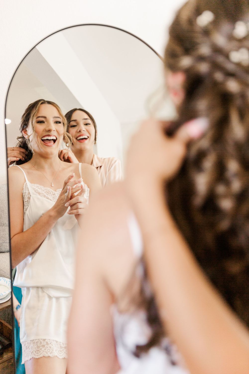 Two people share laughter while getting ready, reflected in a round mirror.