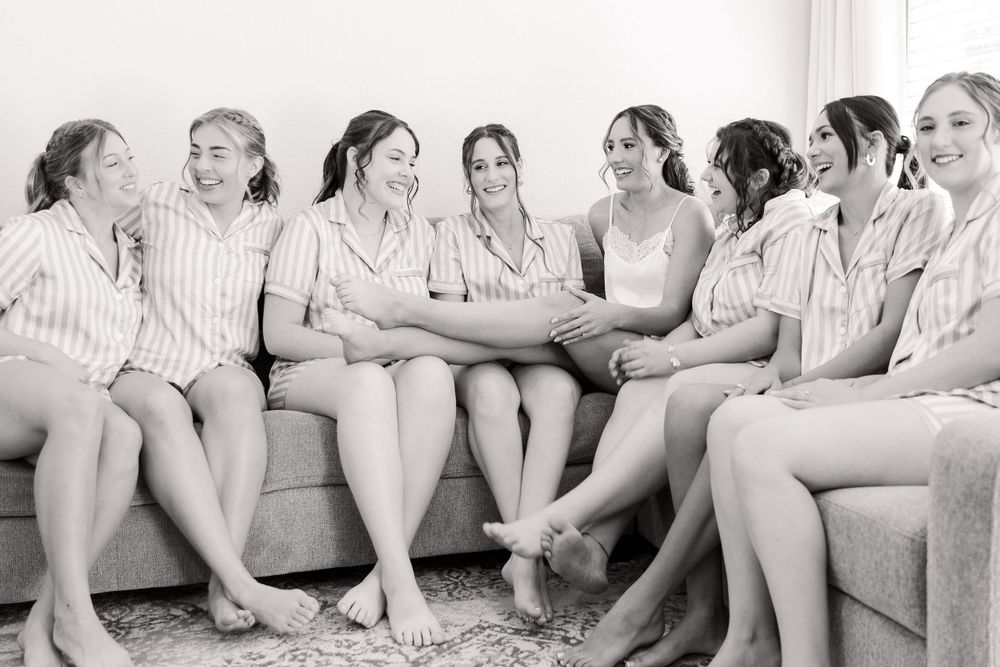 A candid black and white photo captures bridesmaids sharing laughs on a couch.