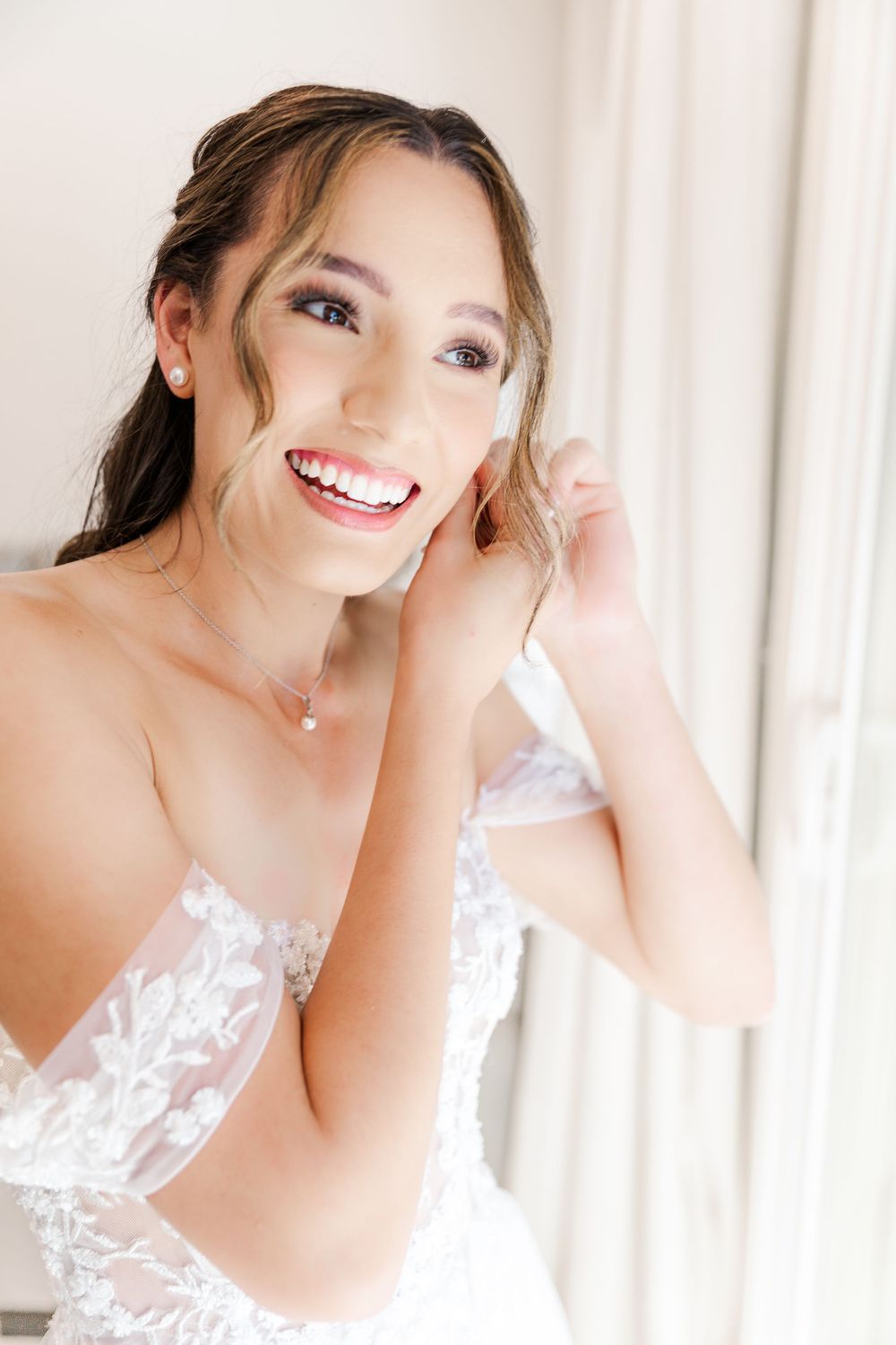 A radiant smile shines through as final wedding preparations take place in a bright room.