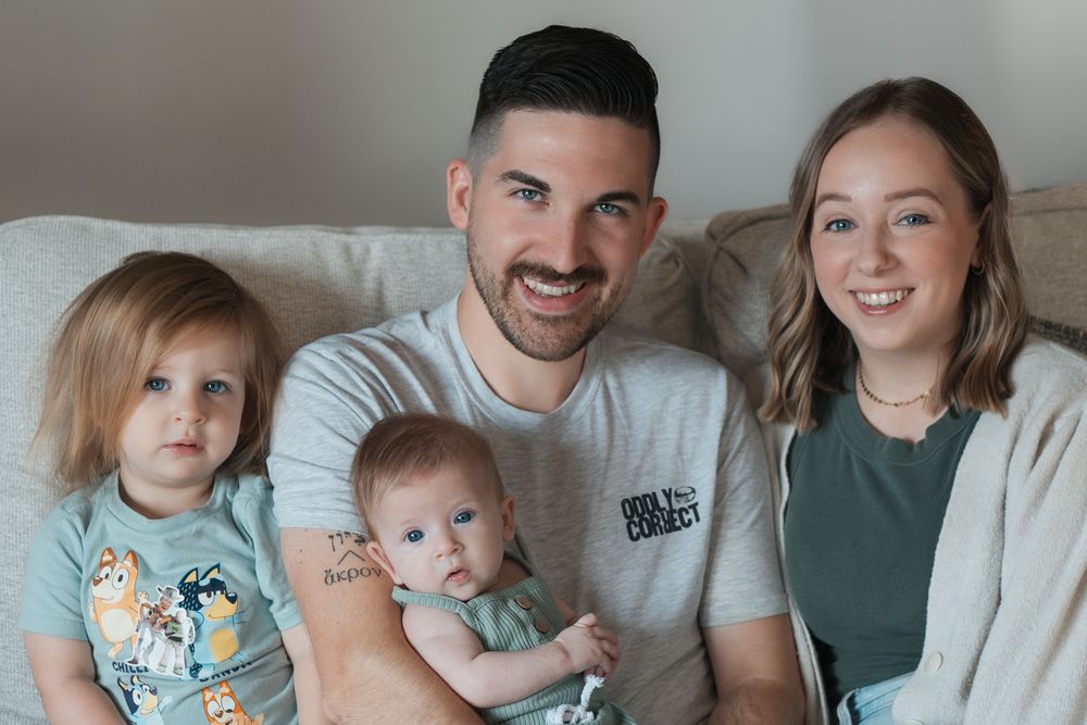 Happy family of four sitting together on a couch for a casual indoor portrait session in Cuyahoga Falls, Ohio