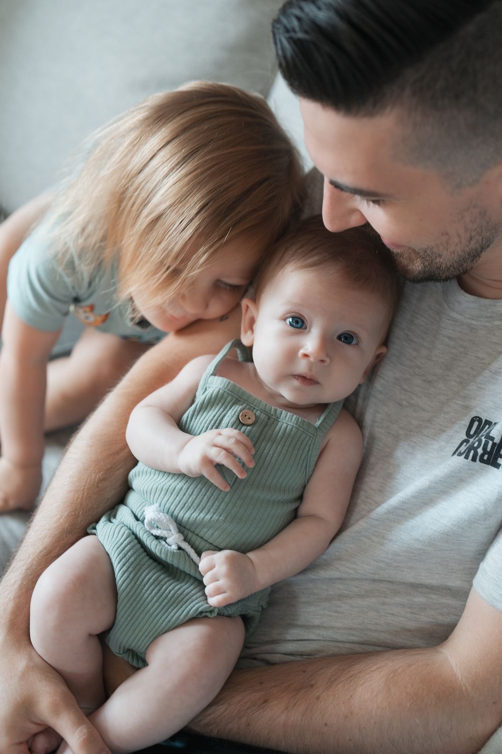 A tender family moment shows a baby in mint green romper being held close with siblings at an indoor newborn session in Cuyahoga Falls, Ohio