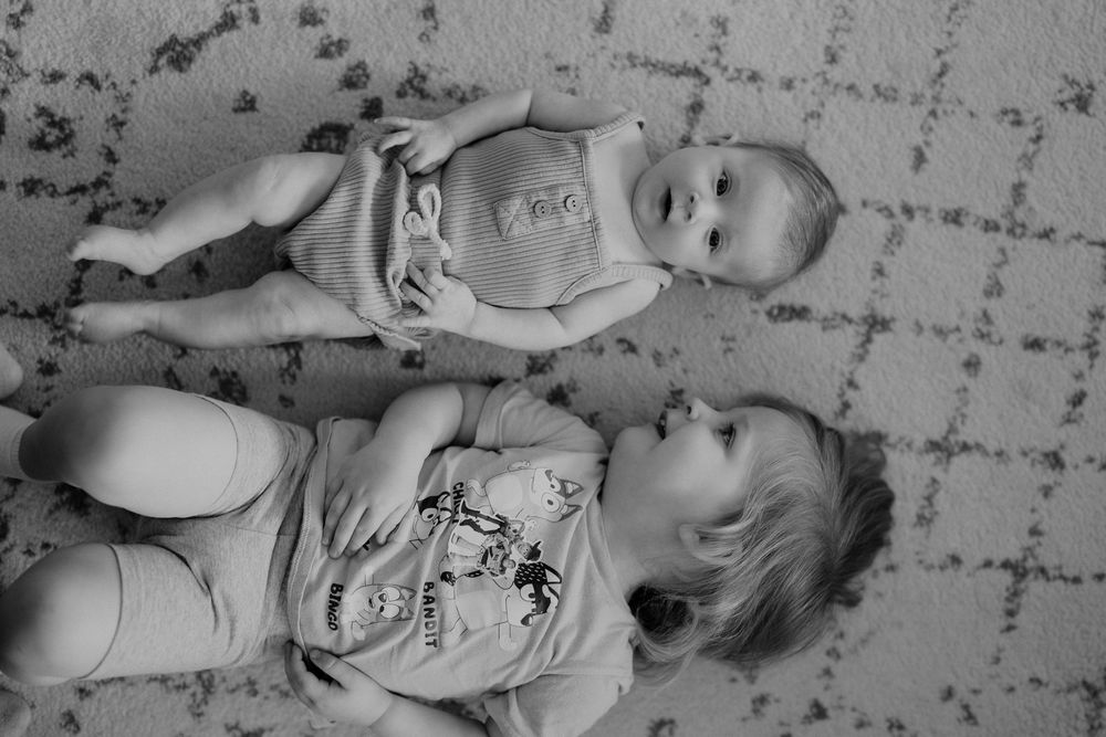 Black and white overhead view of children laying on patterned floor together at an indoor newborn session in Cuyahoga Falls, Ohio