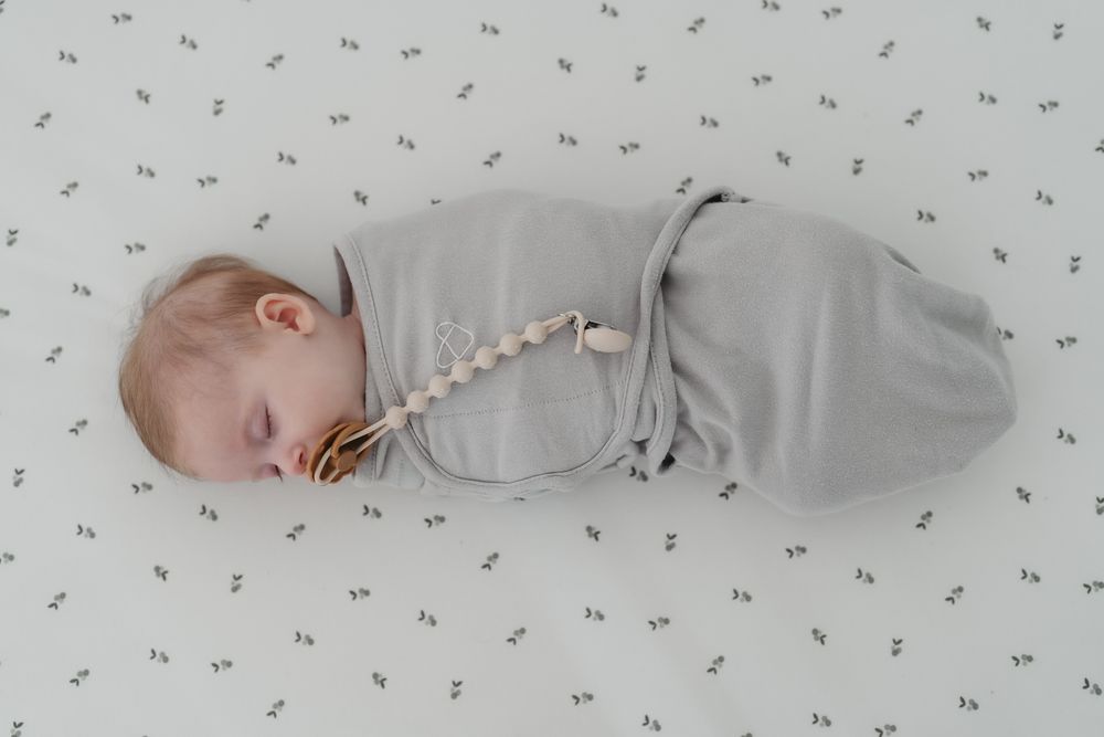 Sleeping infant swaddled in grey wrap on patterned sheet at an indoor newborn session in Cuyahoga Falls, Ohio