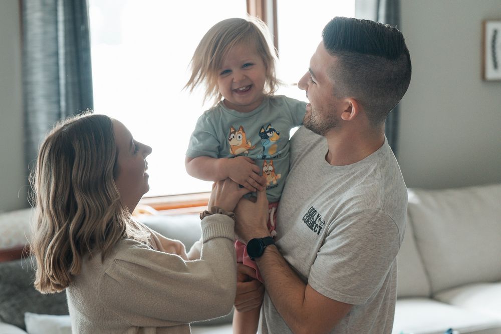 A young family shares a joyful moment together in their living room with natural window light at an indoor newborn session in Cuyahoga Falls