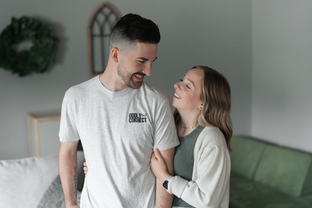 A couple wearing matching white t-shirts share a tender moment together by a wall with decorative wreath at an indoor newborn session in OH