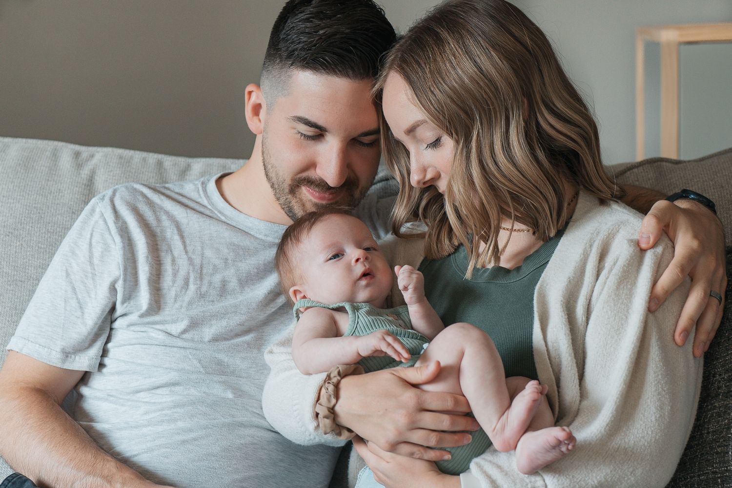 Parents lovingly hold and gaze at their newborn baby while relaxing together on a bed at home.