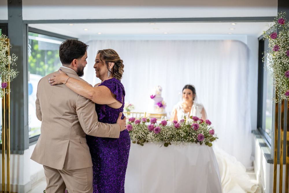 Couple embraces near floral wedding reception table under white draped canopy during daytime celebration.