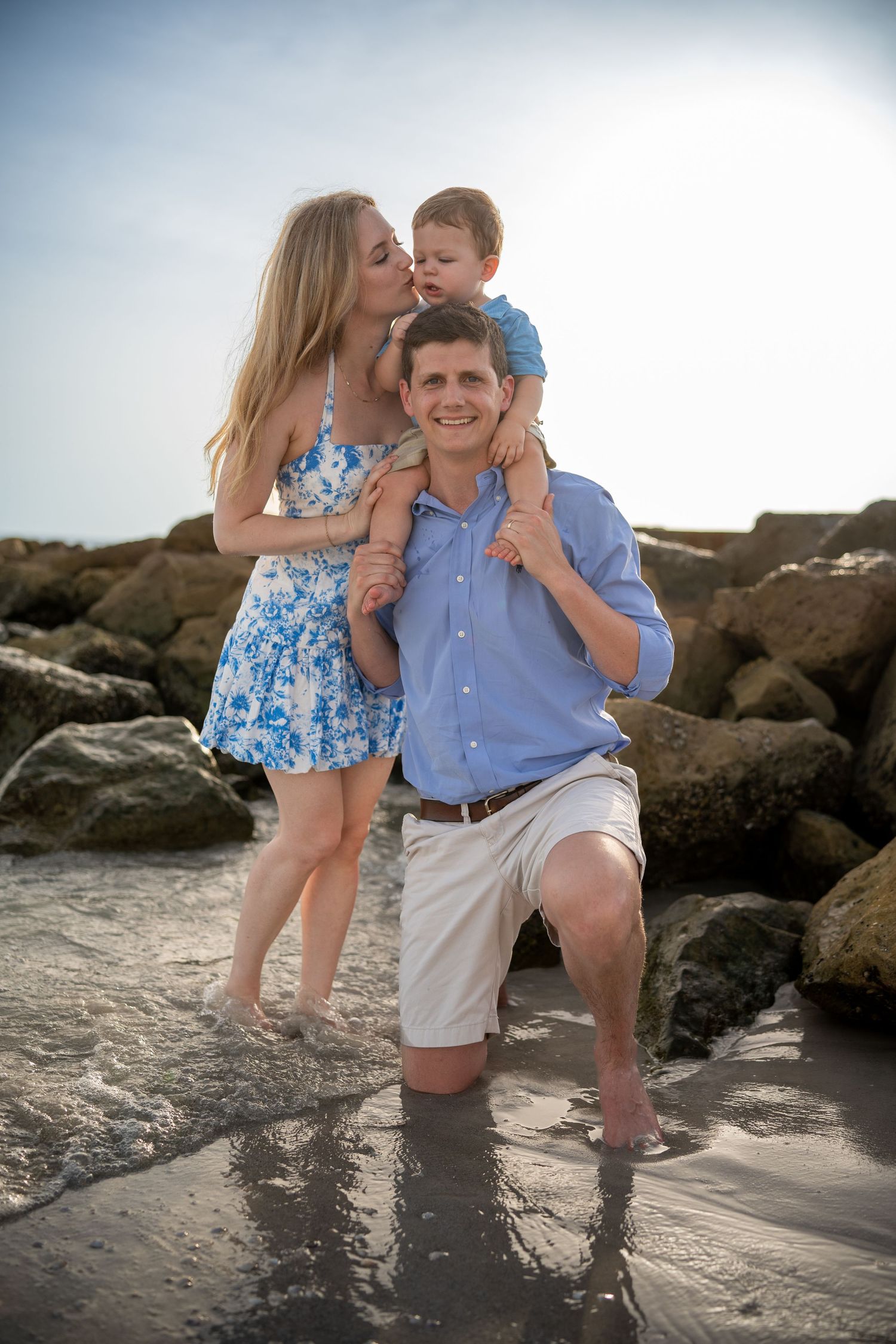 A family plays together on rocky beach at sunset while wearing coordinated blue and white outfits.