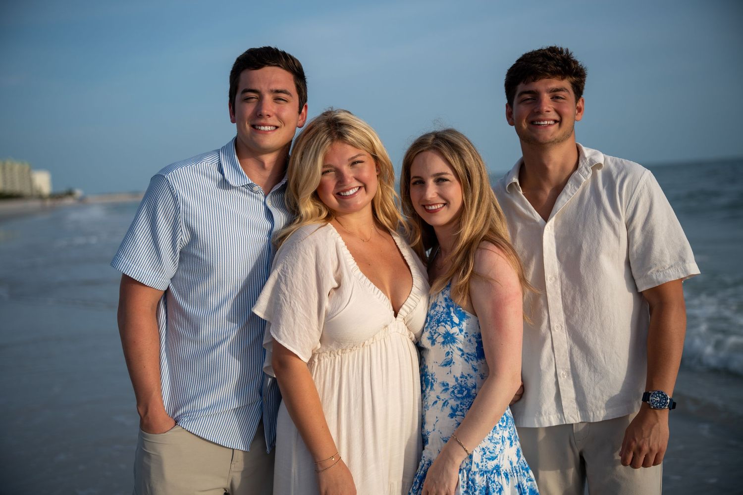 Family in coordinated white and blue outfits posing together on a sunny beach during sunset for beach portraits.