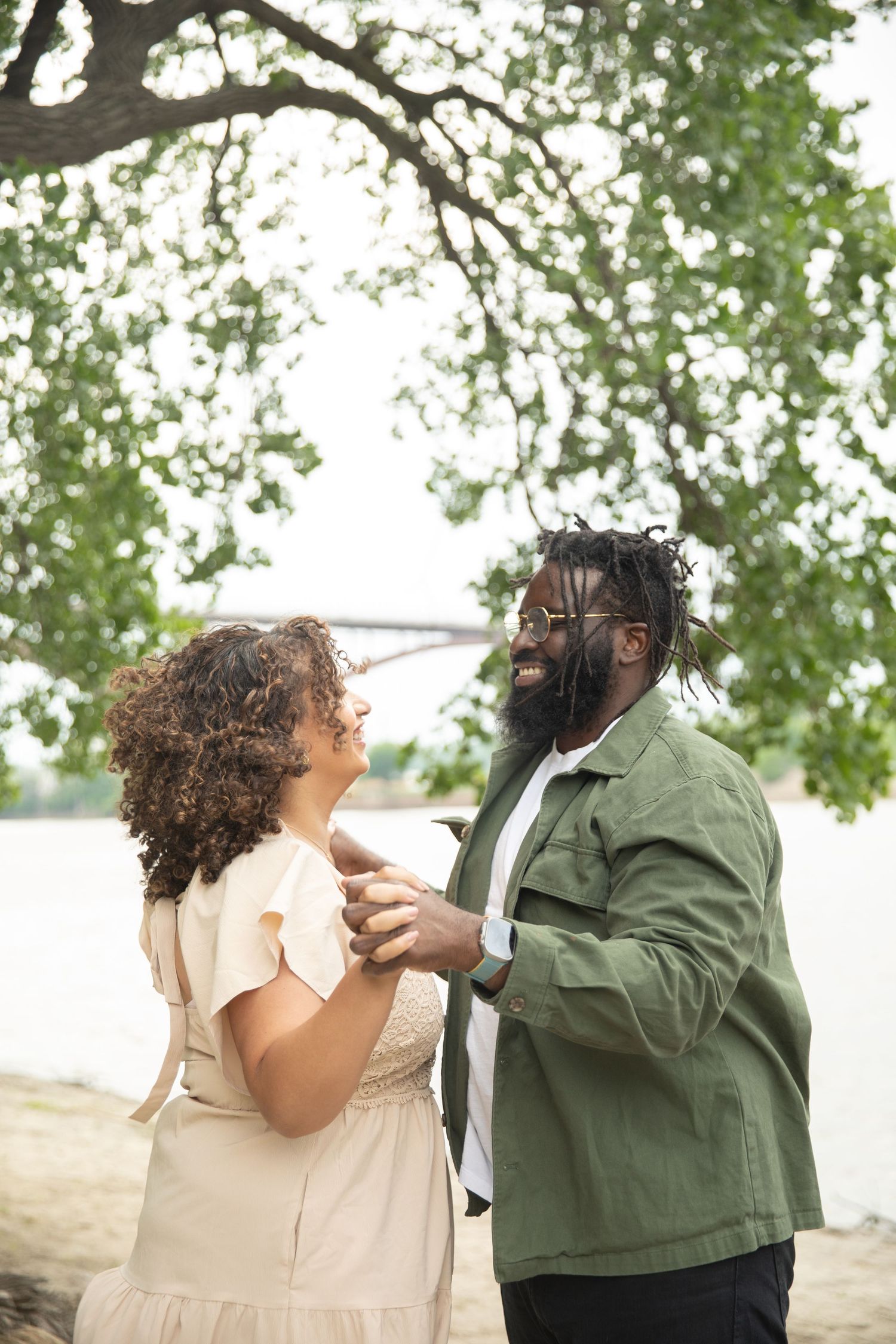 A couple shares an intimate moment together on a beach under tree branches with soft bokeh lighting.
