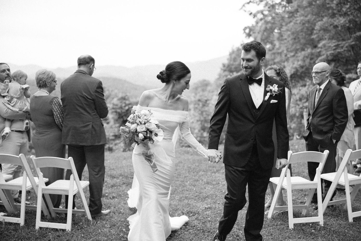 Newlywed couple embraces near stone wall with flowing white veil creating romantic atmosphere.
