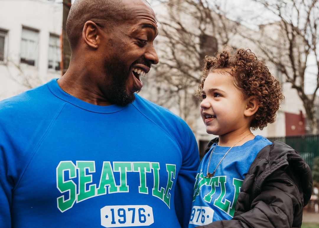 A joyful moment shared between someone wearing a blue Seattle 1976 shirt and a curly-haired child in matching blue.