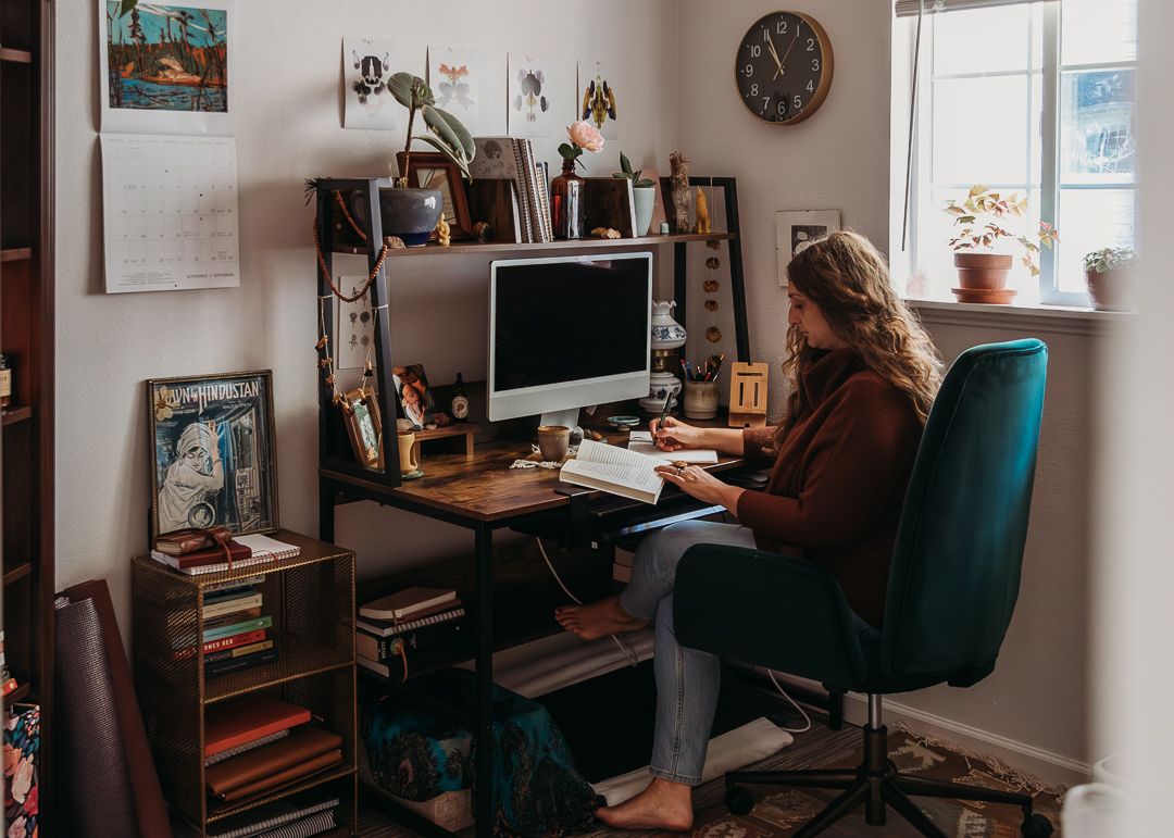 A cozy home office setup with a desk, computer monitor, bookshelves and natural light coming through the window.